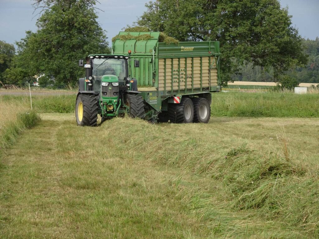 Ladewagen Ein John Deere Traktor mit Krone Ladewagen bei der Grasernte auf einer Wiese zur Förderung von Biodiversität und Ressourcenschutz in der Agrarlandschaft.